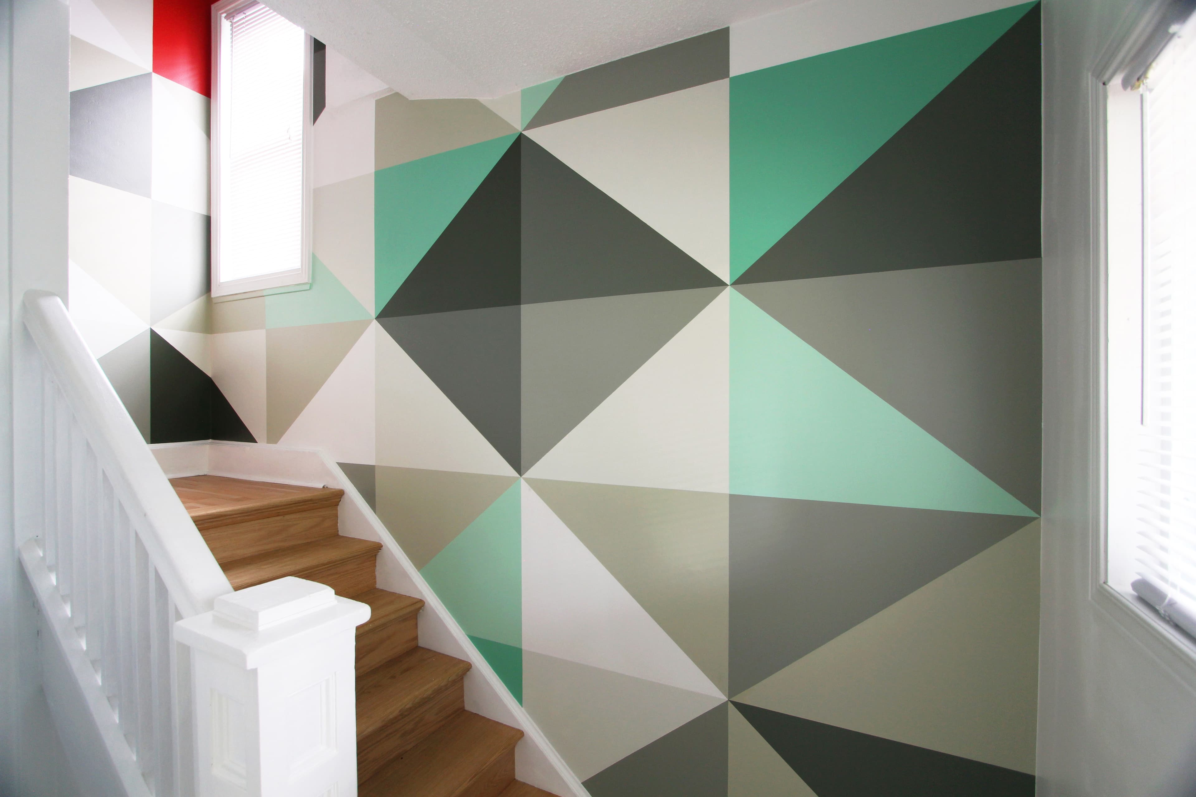 Green and grey triangulated geometric mural by Elevate Form along a bright stairwell with a white railing and wood steps.
