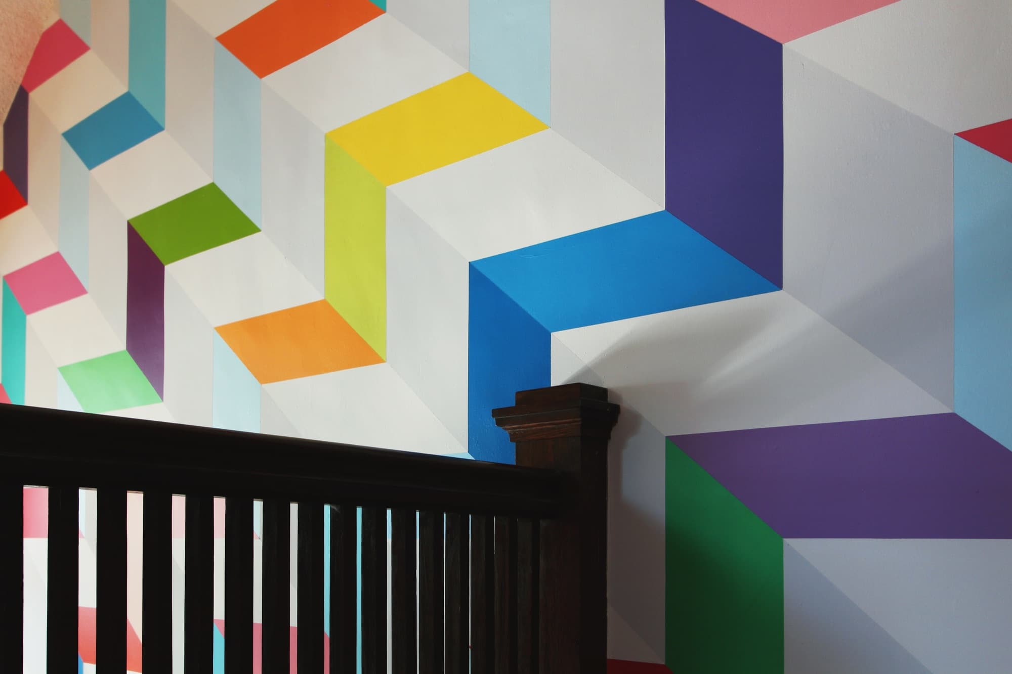 Chromatic Ascent — wide view of the upper wall with the dark oak banister cutting across the foreground.